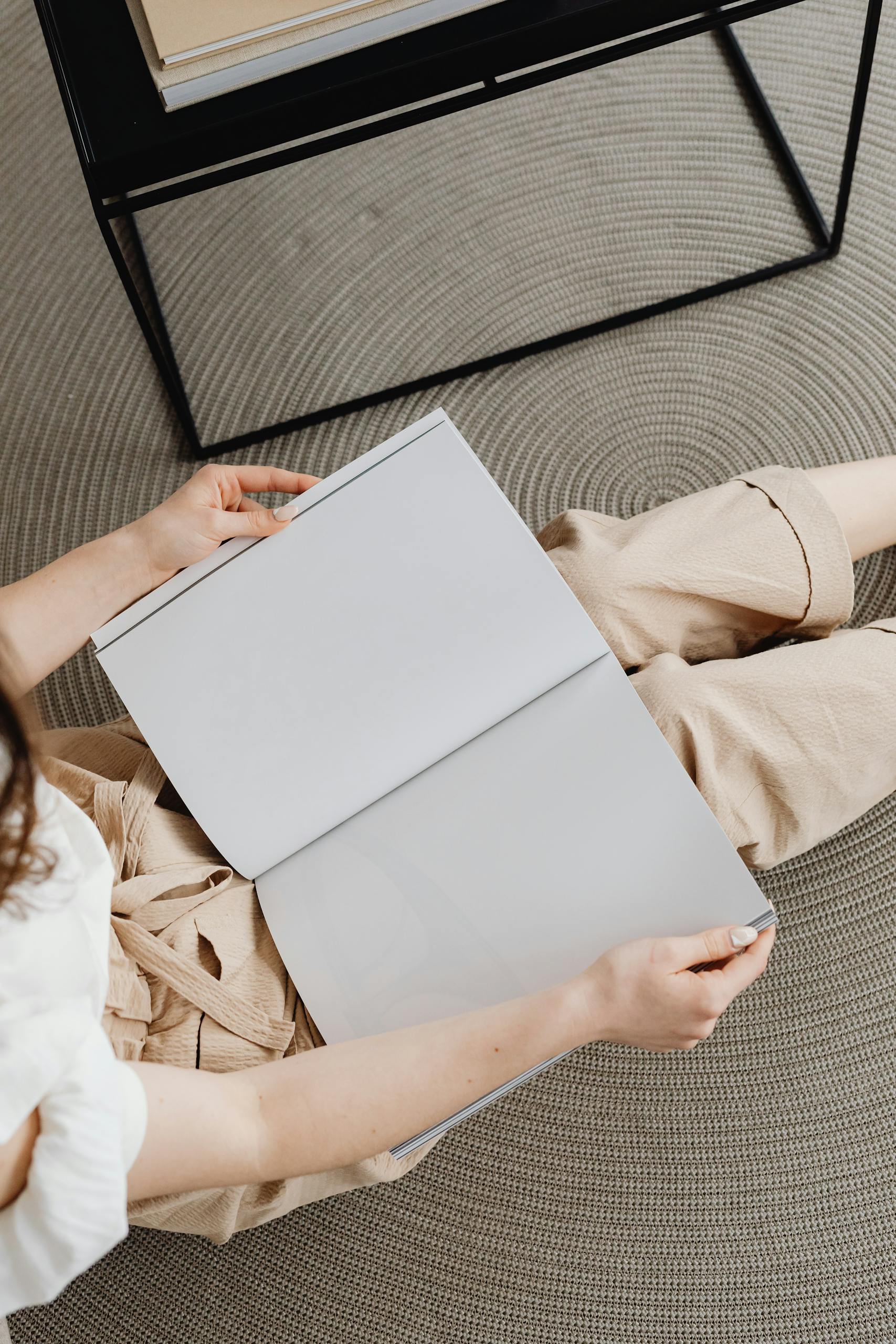 Overhead shot of a person sitting on a carpet, holding an open blank magazine.