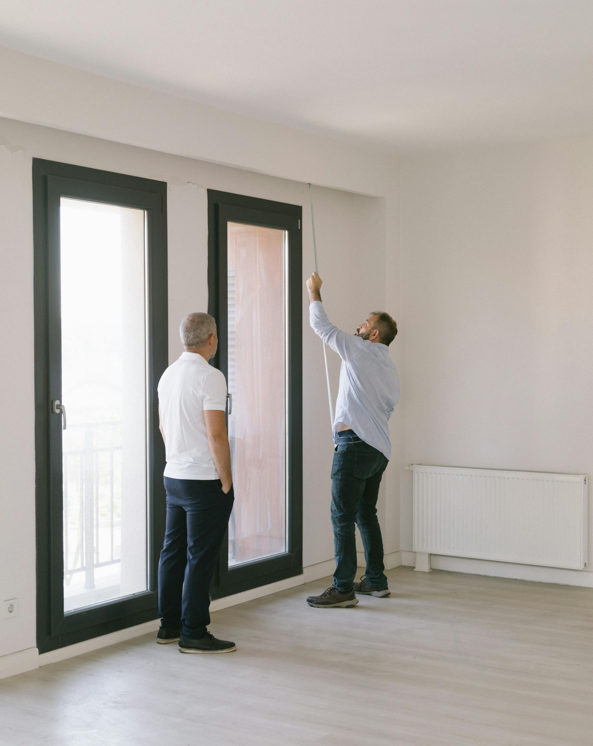 Two men measuring window dimensions in a bright Istanbul apartment.